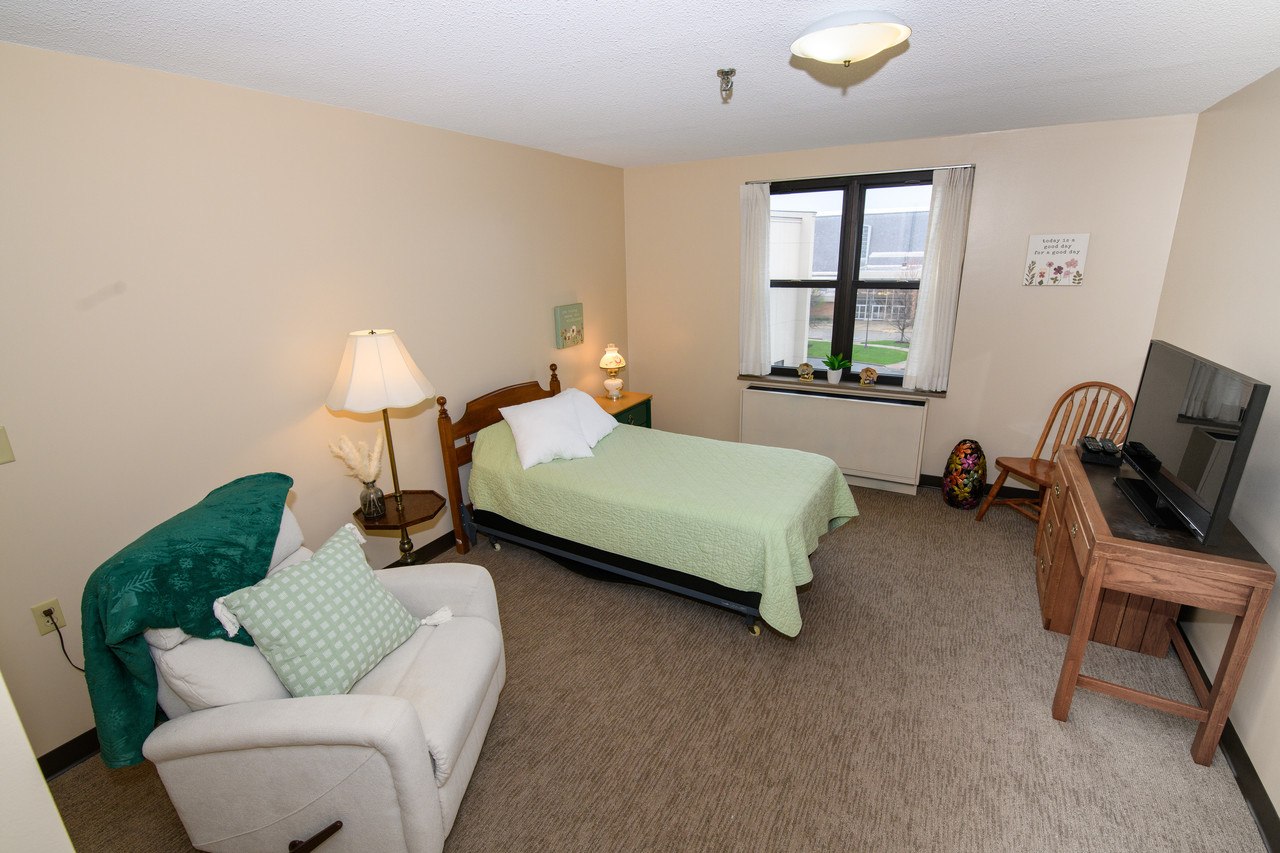 Studio Assisted Living Apartment - Cozy room with bed, sitting area, TV, and large window